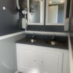 image shows the interior of a luxury restroom trailer, specifically a vanity area with two sinks and mirrors, likely part of a larger unit like a 6-stall luxury restroom trailer